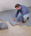 Contractors installing basement subfloor tiles and matting on a concrete basement floor in Watertown, New York